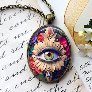 May include: A gold chain necklace with a round glass pendant featuring a colourful eye surrounded by flowers. The pendant is set in a bronze frame. The text "SLR Free Spirit Jewelry" is visible in the bottom right corner of the image.