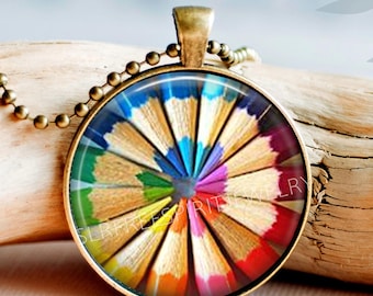 May include: A round pendant necklace featuring a colorful radial pattern of sharpened colored pencil tips arranged in a circle. The pendant has a bronze-toned metal frame and is attached to a matching bronze-toned ball chain necklace.
