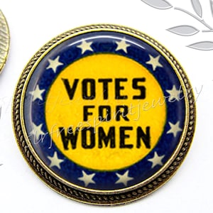 May include: A round, bronze-colored pin with a blue and yellow design. The pin features a white circle with the text "Votes for Women" in black lettering. The circle is surrounded by a ring of white stars on a blue background.