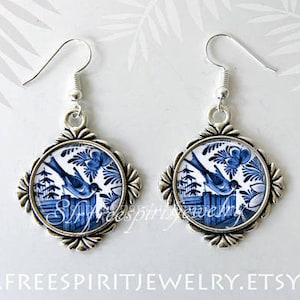 May include: A pair of silver earrings with blue and white porcelain pendants featuring a bird perched on a fence. The porcelain is decorated with a floral design.