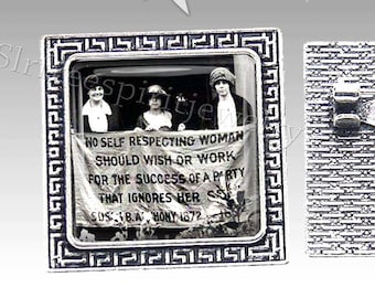 May include: A silver-toned brooch with a black and white photo of three women holding a banner that reads "NO SELF RESPECTING WOMAN SHOULD WISH OR WORK FOR THE SUCCESS OF A PARTY THAT IGNORES HER SUS. B.A. HONY 1872". The brooch is in a square frame with a Greek key design.