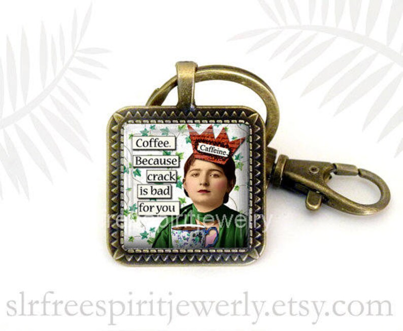 May include: Square keychain with a bronze finish. The image features a vintage portrait of a person wearing a crown with the word "Caffeine" and holding a teacup. Text on the keychain reads "Coffee. Because crack is bad for you."