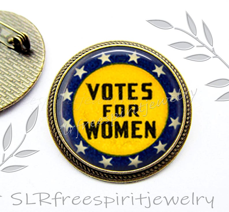 May include: A round, bronze-colored pin with a blue and yellow design. The pin features a white circle with the text "Votes for Women" in black lettering. The circle is surrounded by a ring of white stars on a blue background.