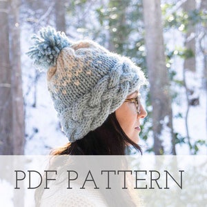 May include: A light blue and cream-colored knitted hat with a cable knit design and a pom-pom. The hat is worn by a person with glasses, with the text "PDF PATTERN" at the bottom of the image. The background is a snowy forest.