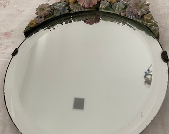 Puede incluir: Un espejo redondo con un marco de diseño floral. El marco está hecho de cerámica y presenta flores rosas, verdes y amarillas.