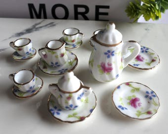 May include: A miniature porcelain tea set with floral designs in shades of pink, blue, and green. The set includes a teapot, creamer, sugar bowl, four teacups, and four saucers.