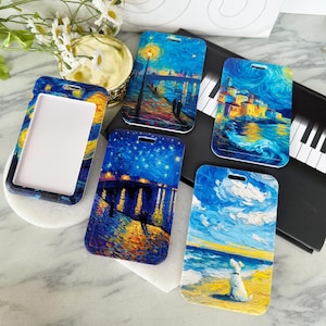 May include: A collection of ID badge holders and a badge holder case featuring famous paintings. The artwork includes a starry night scene, a coastal town, and a dog on a beach. The badge holder case has a white interior.
