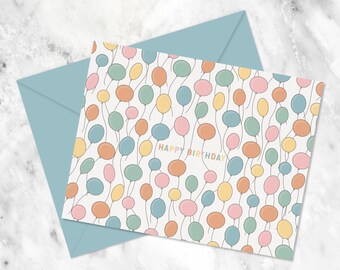 May include: A white card with a colorful balloon pattern and the text "HAPPY BIRTHDAY" in rainbow colors.