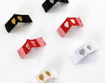 May include: Six different fabric labels with heart designs. The labels are in black, white, red, and beige. The hearts are in gold, silver, and white.