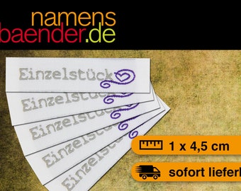 May include: White fabric labels with the word "Einzelstück" in gray, with a purple heart design. The labels are 1 cm x 4.5 cm. The image also includes the website name "namensbaender.de" in red, orange, and green.