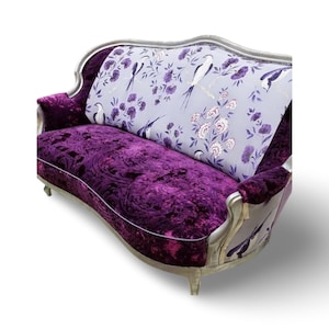 May include: A silver and purple velvet sofa with a floral and bird patterned fabric on the back. The sofa has a curved back and a curved seat.