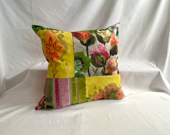 May include: A square pillow with a patchwork design featuring floral patterns in shades of pink, yellow, green, and red. The pillow has a velvet border.
