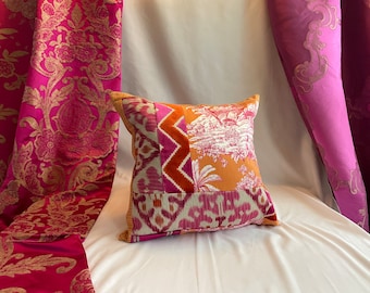 May include: A patchwork pillow with a variety of patterns and colors, including pink, orange, white, and brown. The pillow is sitting on a white surface with pink fabric behind it.