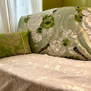 May include: A light green sofa with a floral pattern and a green cushion. The sofa is covered in a white and beige patterned throw.