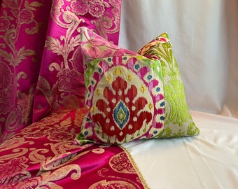 May include: A colorful throw pillow with a pink, red, blue, green, and yellow ikat pattern. The pillow is on a pink and gold patterned fabric.