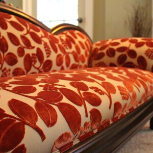 May include: A chaise lounge with a dark wood frame and cream-colored upholstery. The fabric features a repeating pattern of large, stylized red leaves. The design is classic and elegant, suitable for a living room or bedroom.