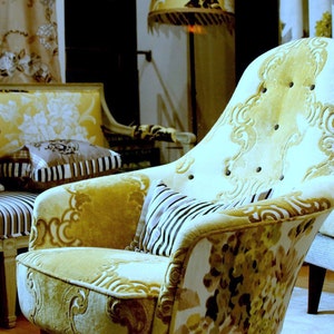 May include: A yellow and white patterned armchair with a floral design. The chair has a high back and a curved seat. The chair is sitting in a room with a lamp and other furniture.