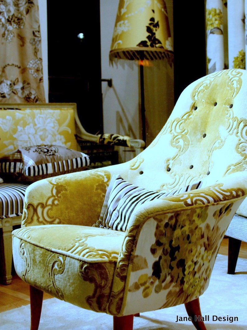May include: A yellow and white patterned armchair with a floral design. The chair has a high back and a curved seat. The chair is sitting in a room with a lamp and other furniture.