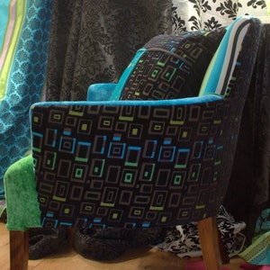 Op de afbeelding: Een zwarte en groene fauteuil met een geometrisch patroon. De fauteuil heeft een hoge rugleuning en een houten frame. De fauteuil is bekleed met een zachte, pluche stof.