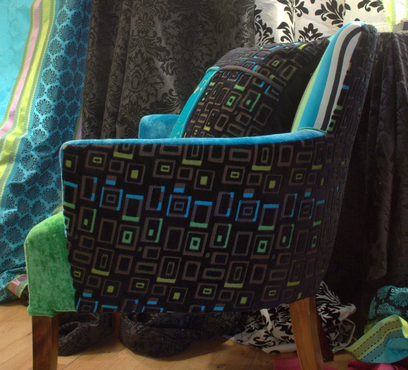 Op de afbeelding: Een zwarte en groene fauteuil met een geometrisch patroon. De fauteuil heeft een hoge rugleuning en een houten frame. De fauteuil is bekleed met een zachte, pluche stof.