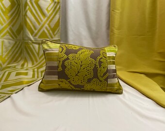 May include: A green and brown patterned throw pillow with a decorative trim. The pillow is on a white surface.