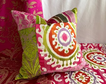 May include: A patchwork pillow with a colorful ikat design. The pillow is made of different fabrics, including velvet, cotton, and silk. The pillow is sitting on a pink and green fabric with a floral pattern.