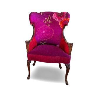 May include: A decorative armchair with a high back and ornate wooden frame. The chair features a vibrant magenta floral pattern on the back and seat, with red accents. The legs are dark brown and curved.