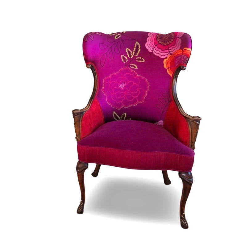 May include: A decorative armchair with a high back and ornate wooden frame. The chair features a vibrant magenta floral pattern on the back and seat, with red accents. The legs are dark brown and curved.