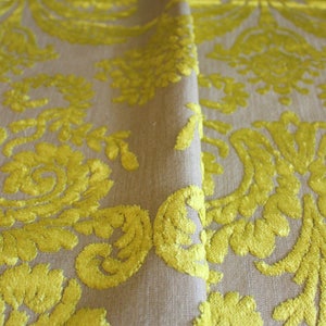 May include: Close-up of a beige fabric with a yellow floral pattern. The fabric has a raised texture, giving it a luxurious feel.