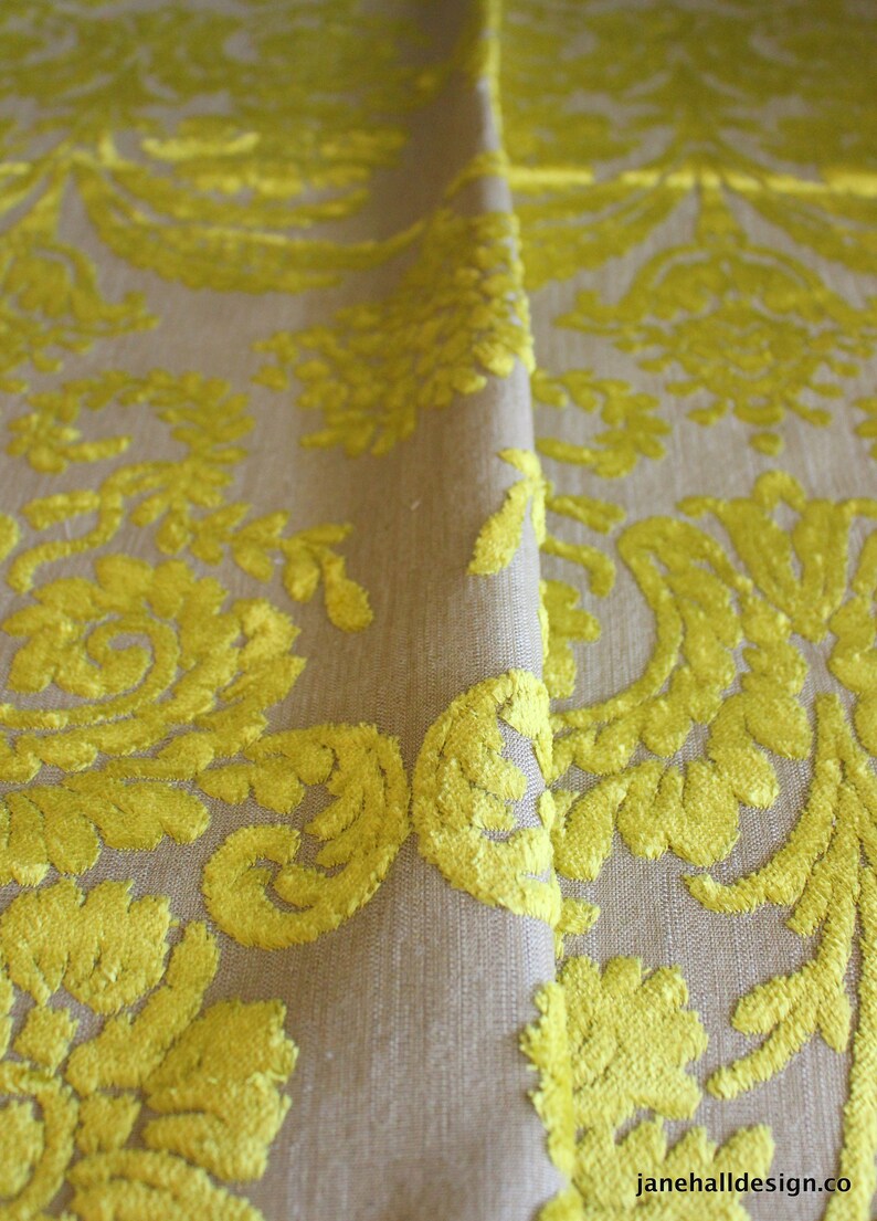 May include: Close-up of a beige fabric with a yellow floral pattern. The fabric has a raised texture, giving it a luxurious feel.