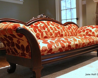 May include: A vintage-style chaise lounge with a dark wood frame and legs. The seat and back are upholstered in a cream-colored fabric with a repeating pattern of orange leaves and berries. The design is elegant and classic.