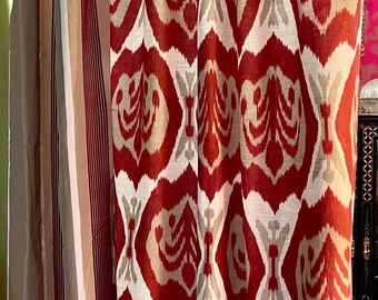 May include: Red, white, and tan patterned curtains with a bold ikat design. The curtains are hanging next to a set of neutral-colored curtains with vertical stripes. Home decor.