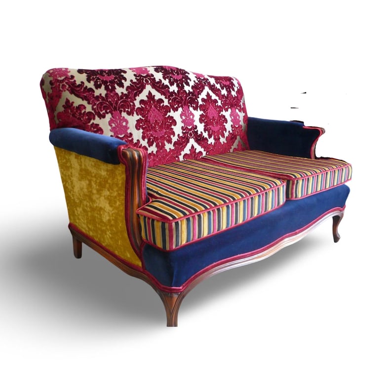 May include: A vintage-style loveseat upholstered in a mix of colorful fabrics. The back is covered in a red and white damask pattern, the sides are yellow, and the seat is striped in various colors. The loveseat has a dark blue velvet trim and wooden legs.