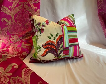 May include: A decorative pillow with a patchwork design featuring floral and geometric patterns in shades of pink, green, and yellow. The pillow is on a white surface.