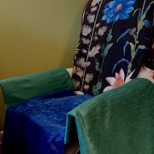 May include: A dark green chair with a floral patterned cushion. The cushion has a large blue flower and smaller pink flowers. The chair is covered in a dark blue velvet fabric and a dark green fabric.