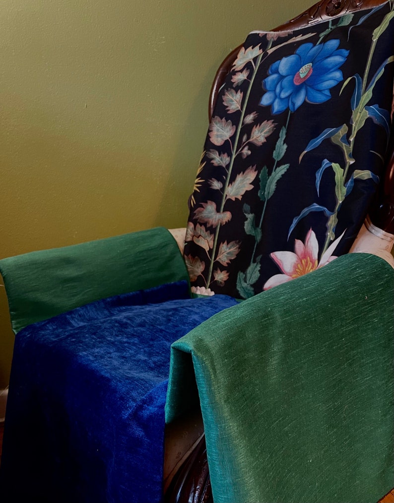 May include: A dark green chair with a floral patterned cushion. The cushion has a large blue flower and smaller pink flowers. The chair is covered in a dark blue velvet fabric and a dark green fabric.