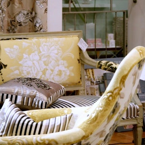 May include: Two chairs with floral patterned upholstery. The chair on the left has a yellow and white floral pattern, while the chair on the right has a white and gold floral pattern. Both chairs have striped cushions.