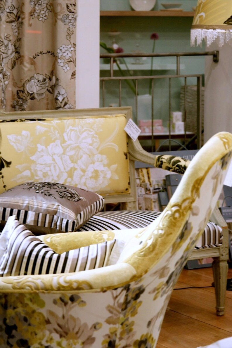 May include: Two chairs with floral patterned upholstery. The chair on the left has a yellow and white floral pattern, while the chair on the right has a white and gold floral pattern. Both chairs have striped cushions.