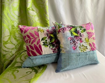 May include: Two decorative throw pillows with floral patterns. One pillow has a pink and green floral pattern with a blue and white geometric border. The other pillow has a blue and white floral pattern with a blue geometric border.