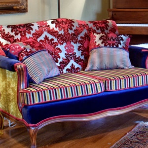 May include: A vintage-style loveseat upholstered in a red and gold damask fabric with blue velvet trim. The loveseat has two striped pillows and a gold and red striped cushion.