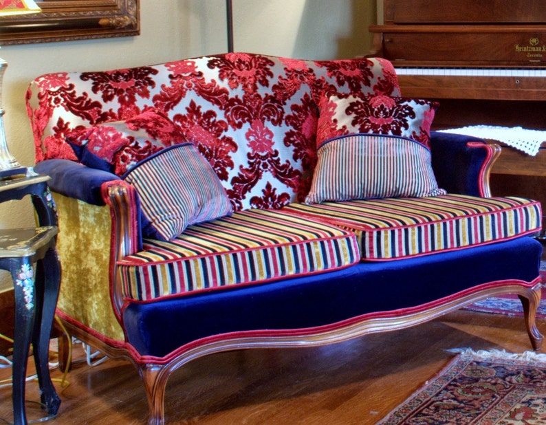 May include: A vintage-style loveseat upholstered in a red and gold damask fabric with blue velvet trim. The loveseat has two striped pillows and a gold and red striped cushion.