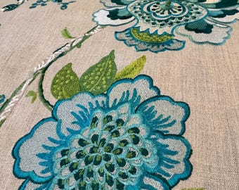 May include: Close-up of embroidered fabric featuring large, stylized flowers in shades of teal, turquoise, and green. The floral design is set against a neutral beige background. The embroidery work is detailed and textured, with visible stitching.