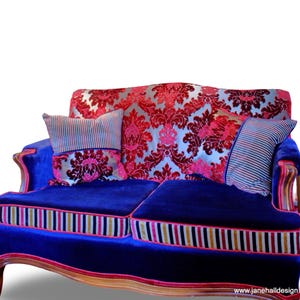 May include: A blue velvet loveseat with a damask patterned back and two pillows. The pillows are striped and have a damask pattern. The loveseat has a wooden frame and a decorative trim.