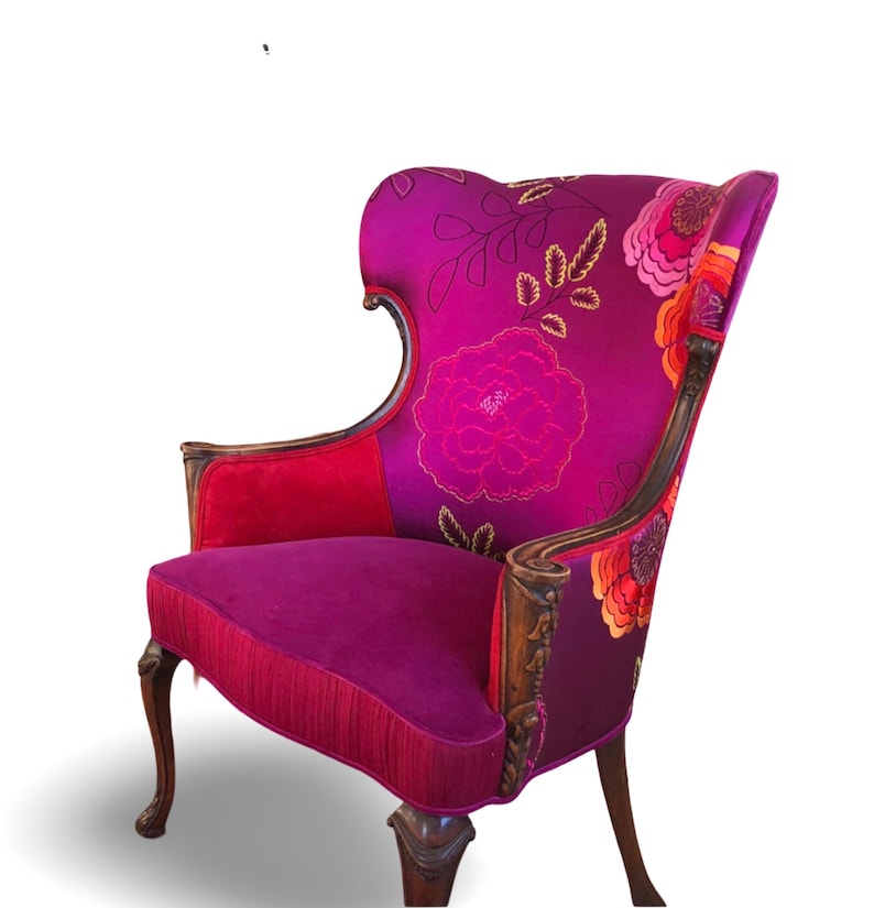 May include: Wingback chair with a high back and floral pattern in shades of pink, red, and purple. The chair has wooden arms and legs with carved details. The seat and back are upholstered in a plush fabric.