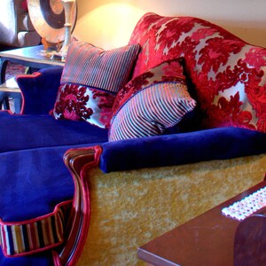 May include: A blue velvet sofa with gold trim and red and white patterned cushions. The sofa has a tufted back and is upholstered in a luxurious fabric.
