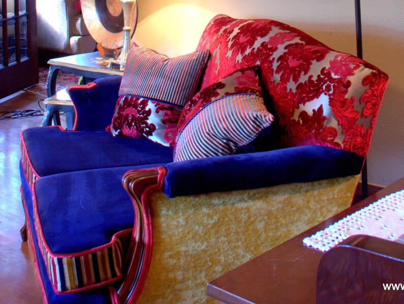 May include: A blue velvet sofa with gold trim and red and white patterned cushions. The sofa has a tufted back and is upholstered in a luxurious fabric.
