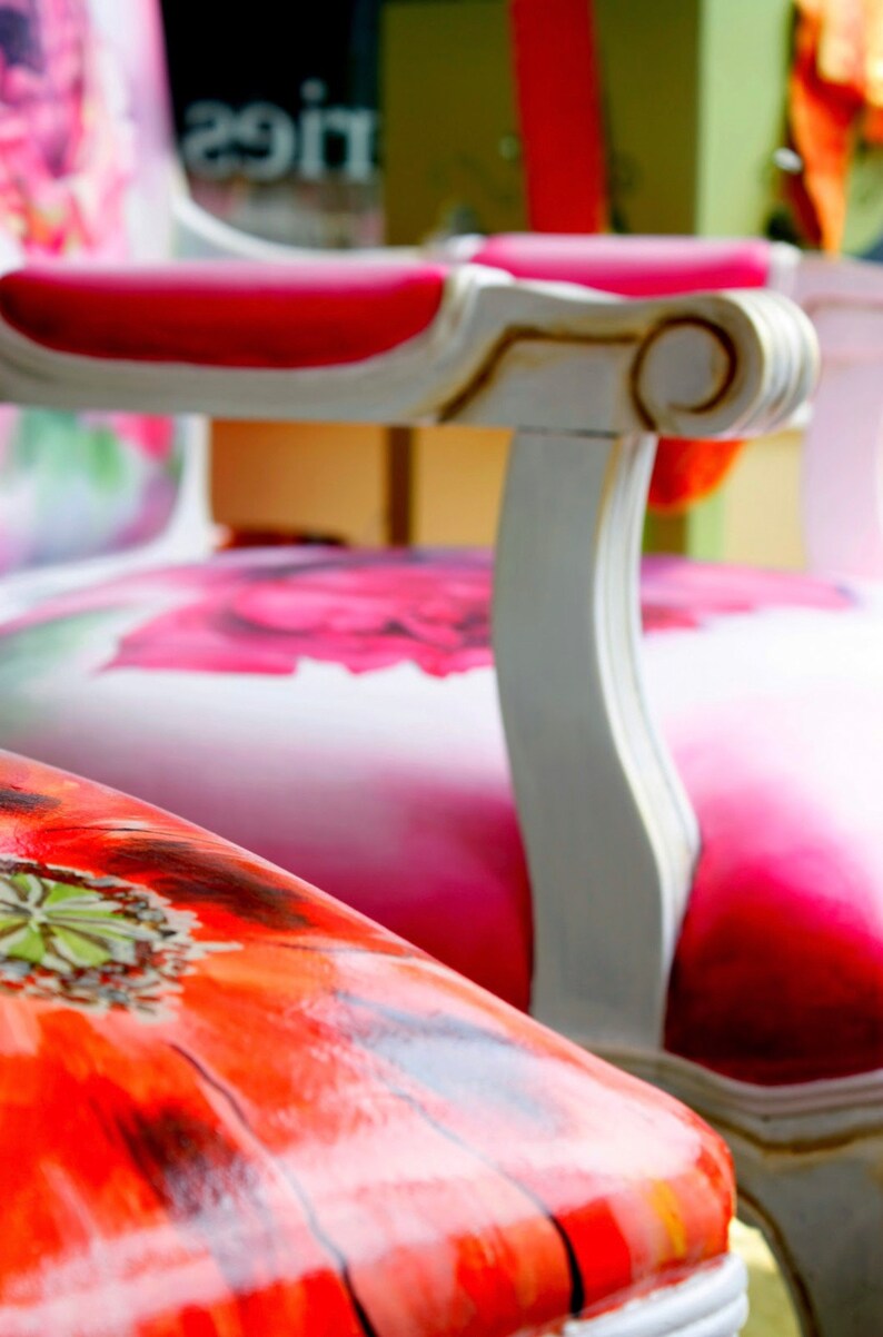 May include: Two white chairs with floral patterned upholstery. The chair in the foreground has a red poppy design, while the chair in the background has a pink floral design.