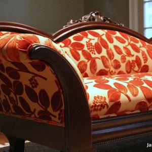 May include: A vintage-style sofa with a dark wood frame and ornate detailing. The seat and back are upholstered in a cream-colored fabric with a vibrant red leaf pattern. The sofa has curved arms and legs, showcasing a classic design.