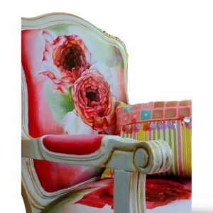 May include: A white, ornate chair with a floral patterned upholstery featuring pink and red roses. The chair has a red cushion and a colorful striped pillow with sequins.