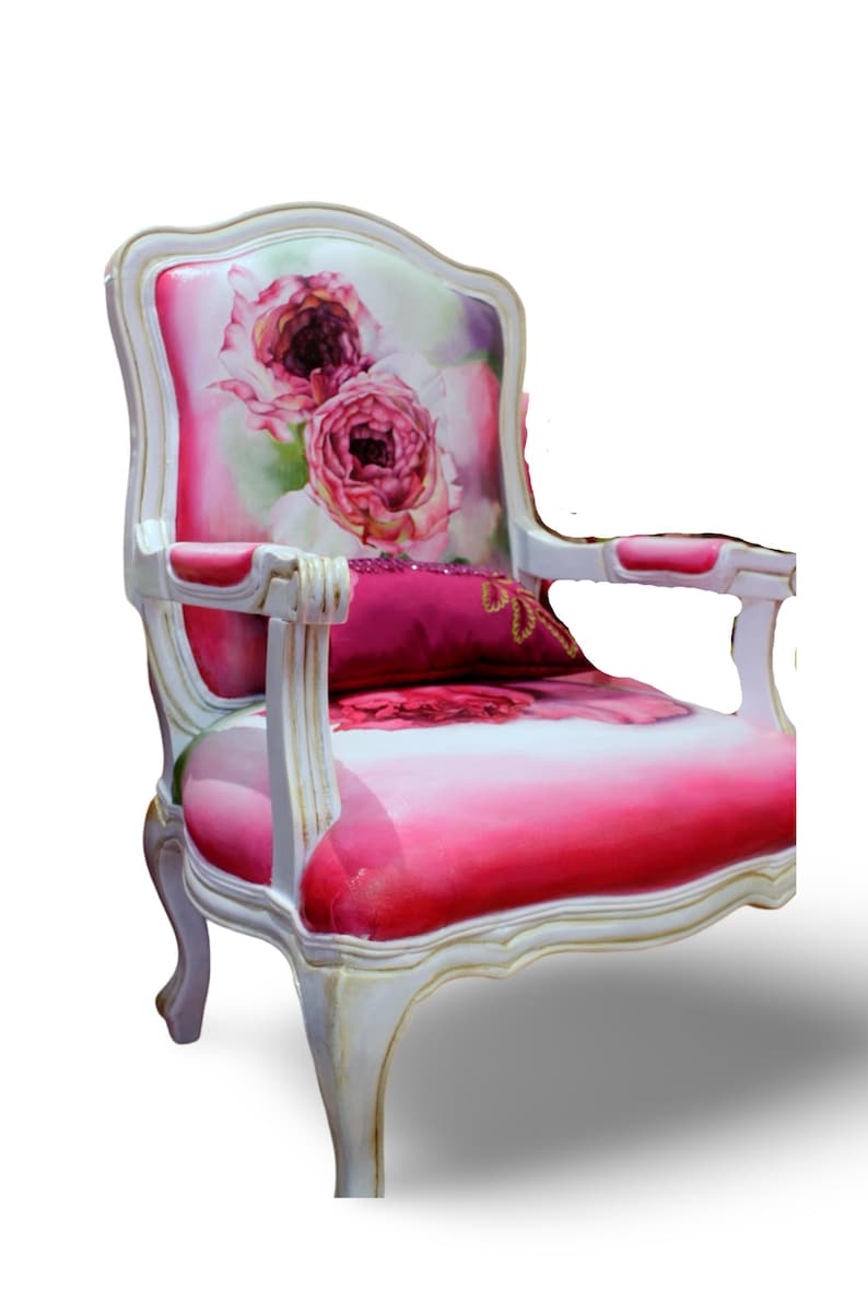 May include: A white and gold armchair with a pink and white floral patterned upholstery. The chair has a curved back and a padded seat with a pink pillow.